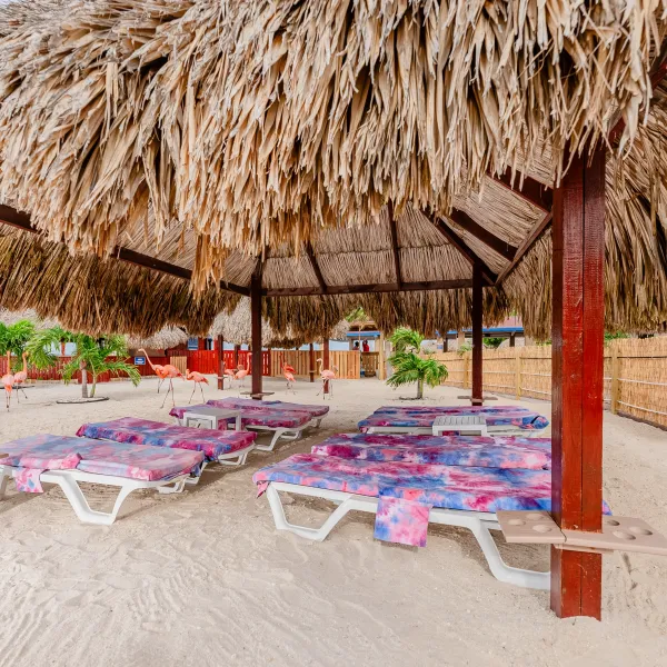 Beach cabana with straw roof, sun loungers, and tropical decor.