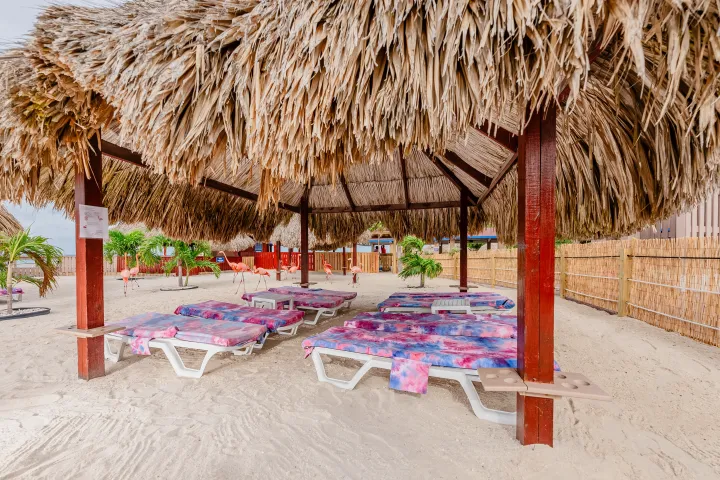 Beach cabana with straw roof, sun loungers, and tropical decor.