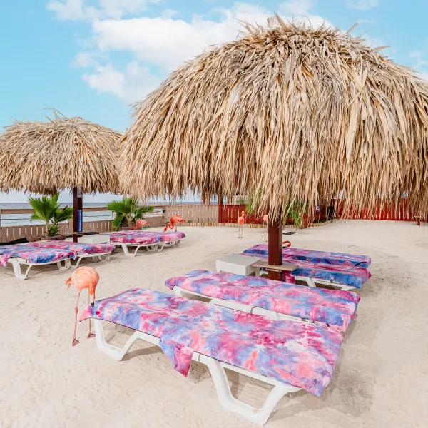 Beach with pink lounge chairs, thatched umbrellas, and flamingos.