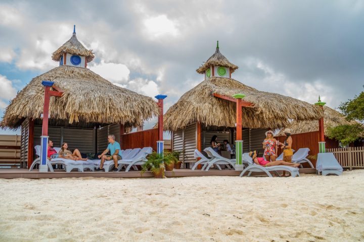 a group of people sitting at a beach umbrella in the sand