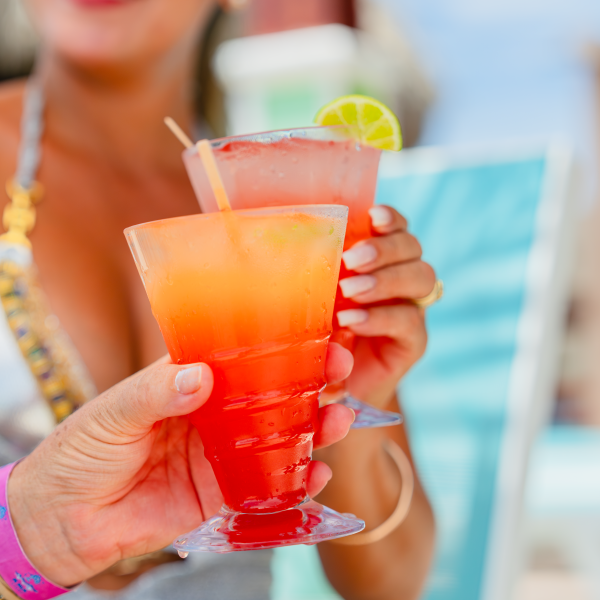 Two people toasting with tropical cocktails at the beach.