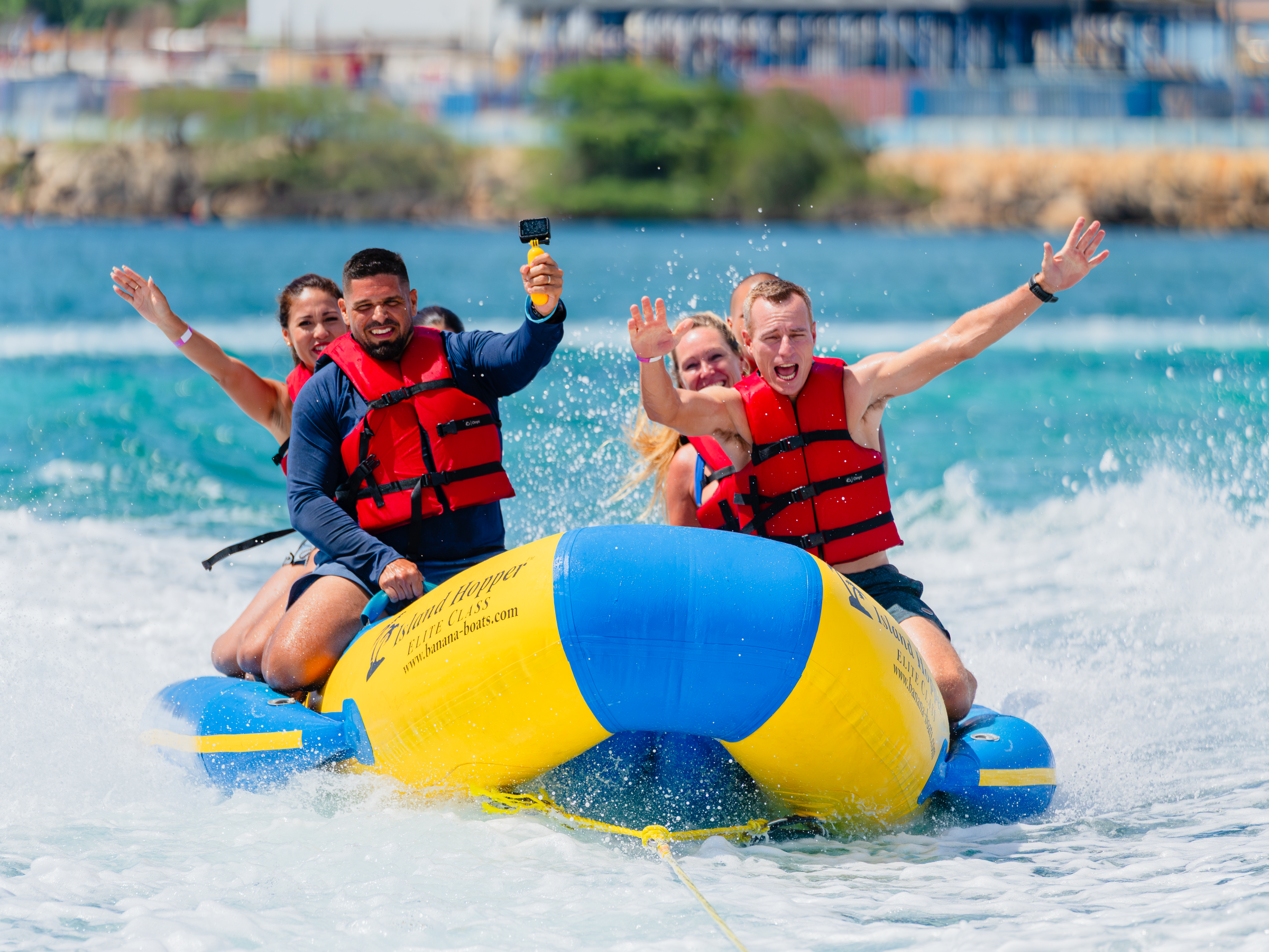 Four people in red life jackets riding a yellow inflatable banana boat on the ocean.