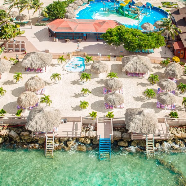 Aerial view of beach resort with cabanas, pools, and clear water.
