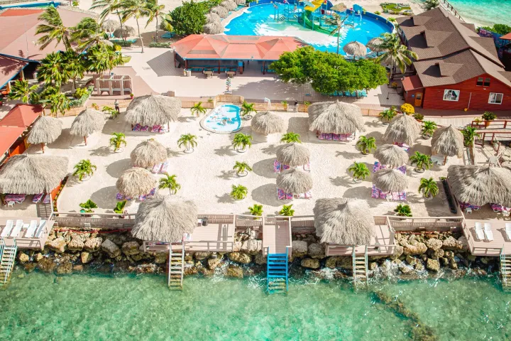 Aerial view of beach resort with cabanas, pools, and clear water.