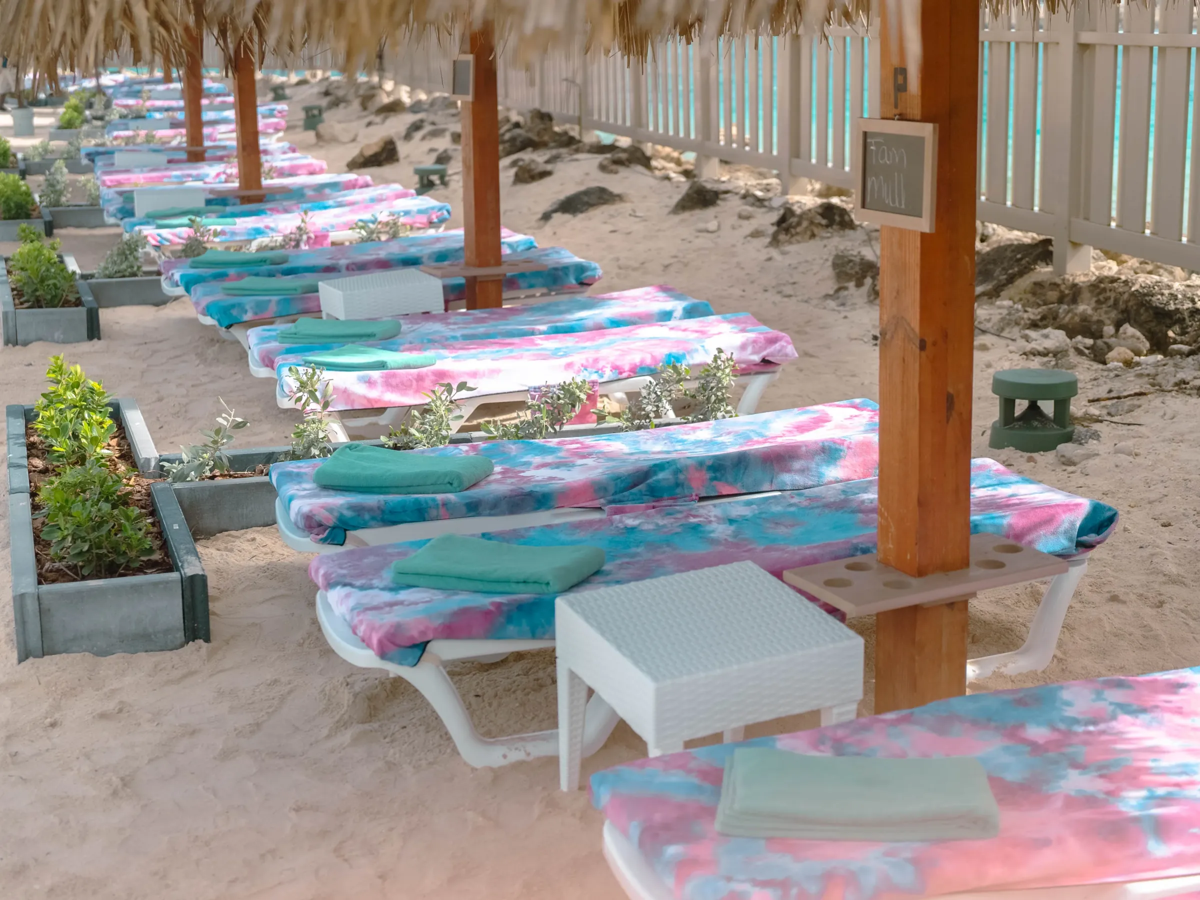Beach loungers with colorful towels under straw umbrellas on sand.