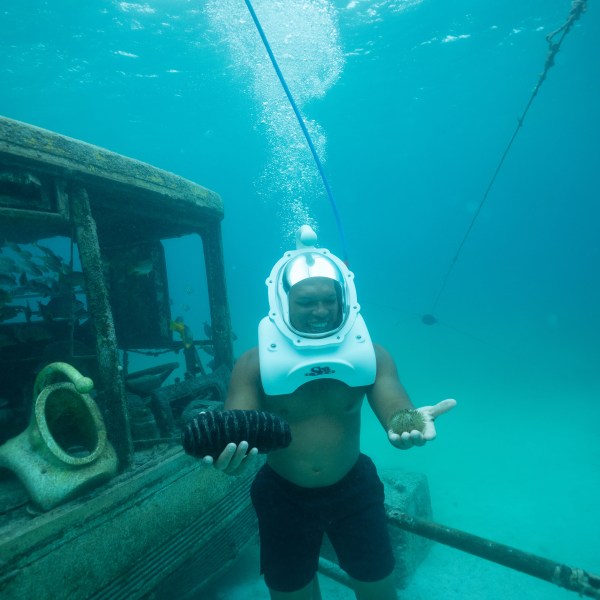 Person underwater with helmet holding sea cucumber, near submerged vehicle.