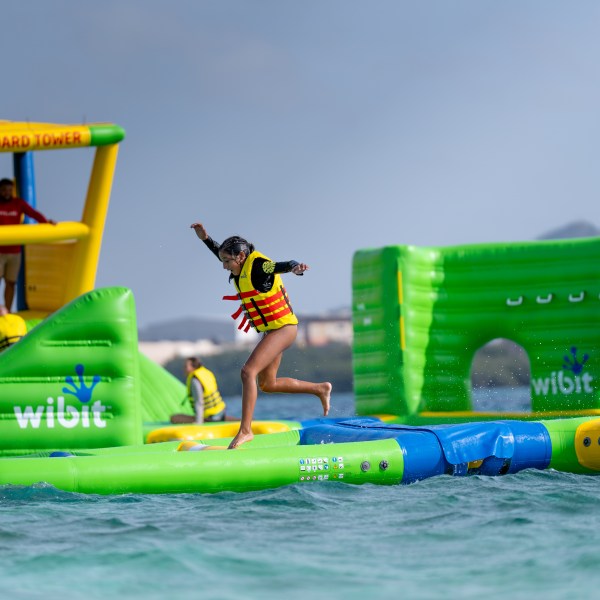 Person in a life jacket jumping on floating obstacle course on water.