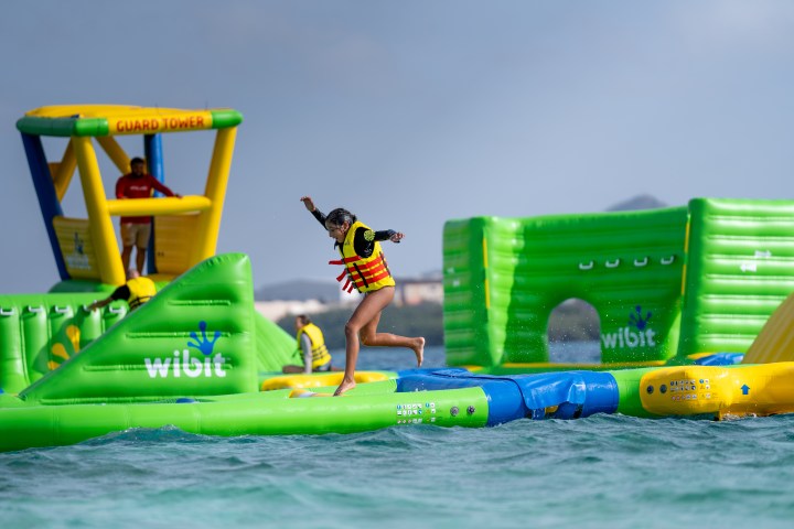Person in a life jacket jumping on floating obstacle course on water.