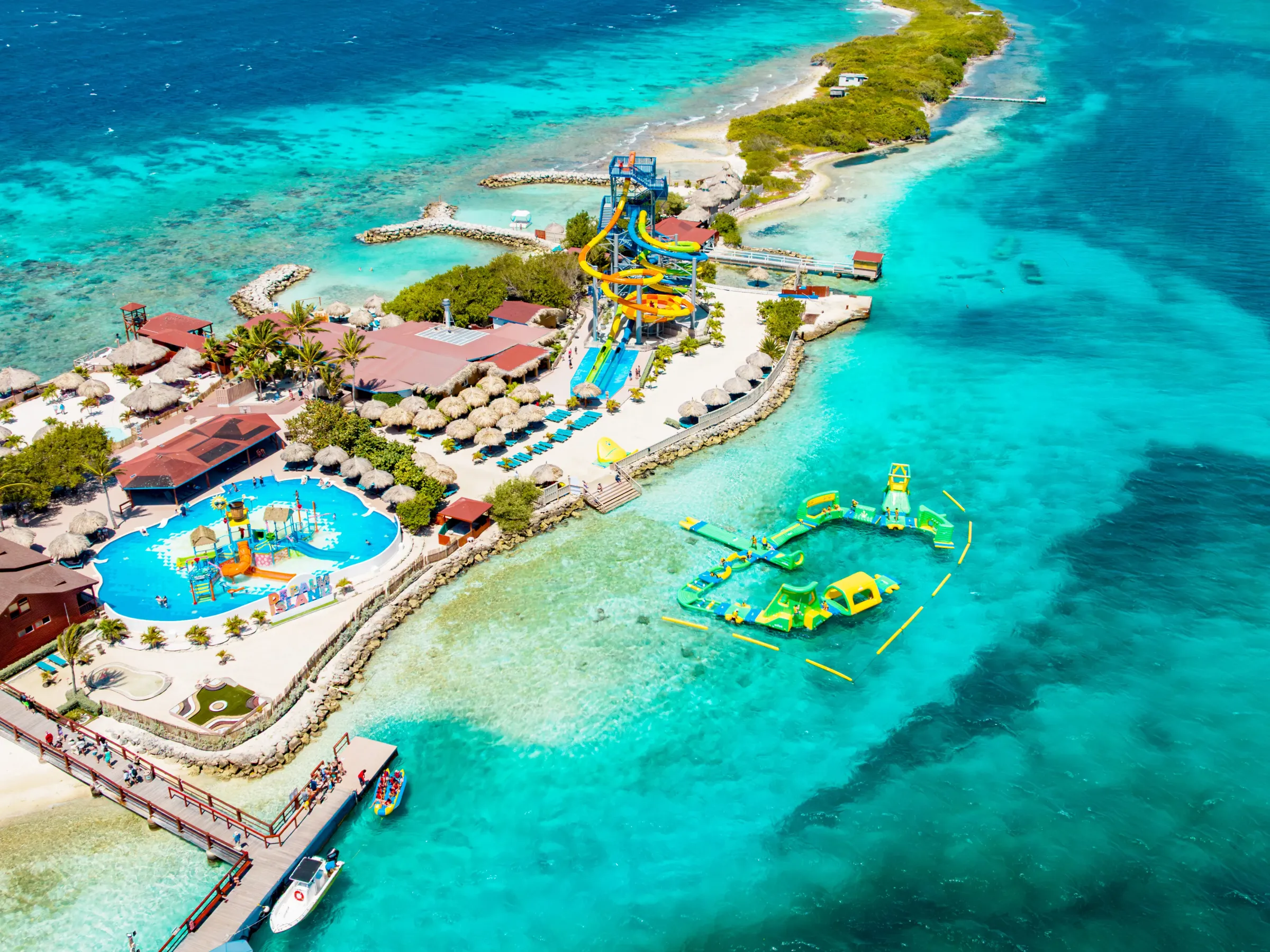 Aerial view of tropical water park with pools, slides, and turquoise sea.