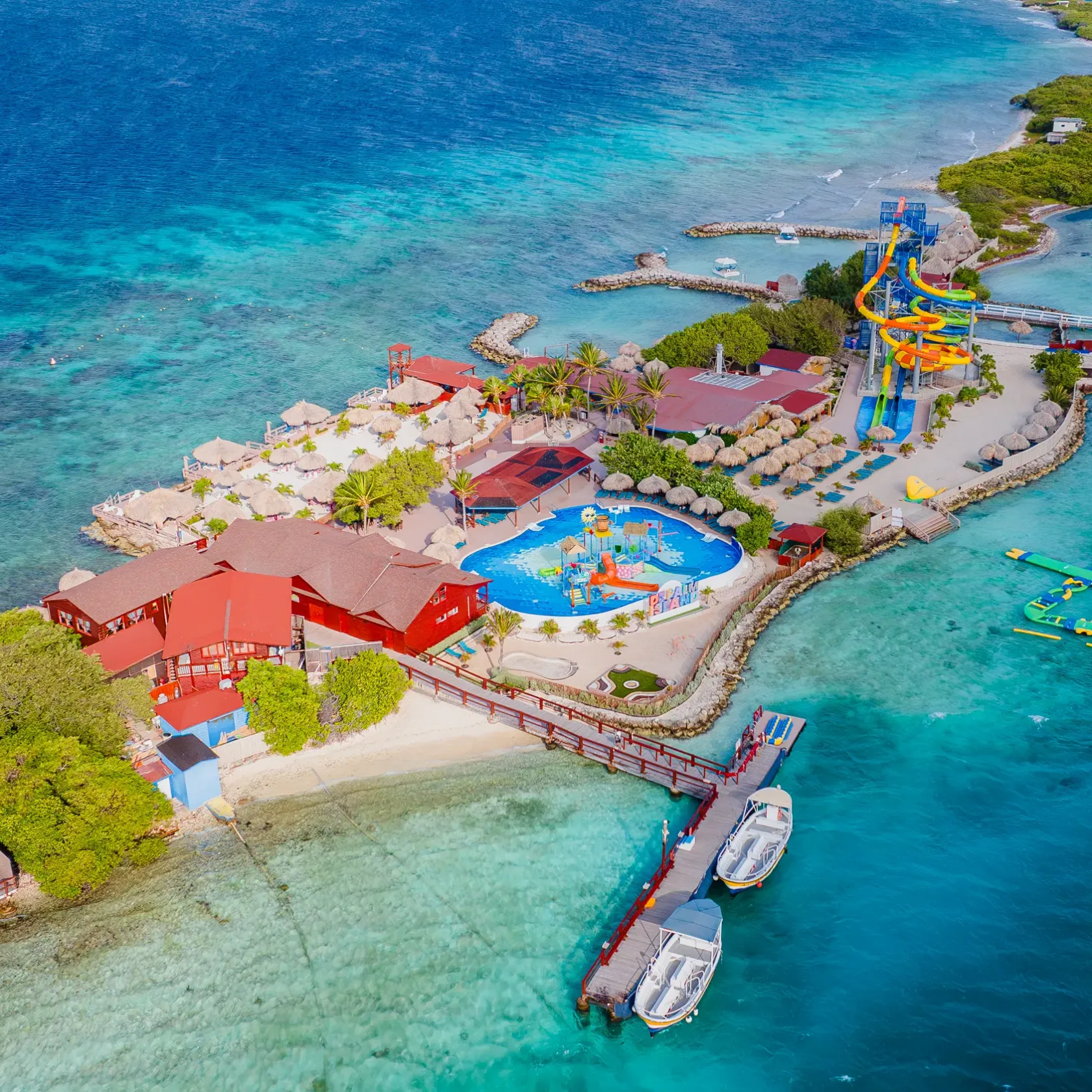 Aerial view of an island resort with pool, water slides, and docked boats.
