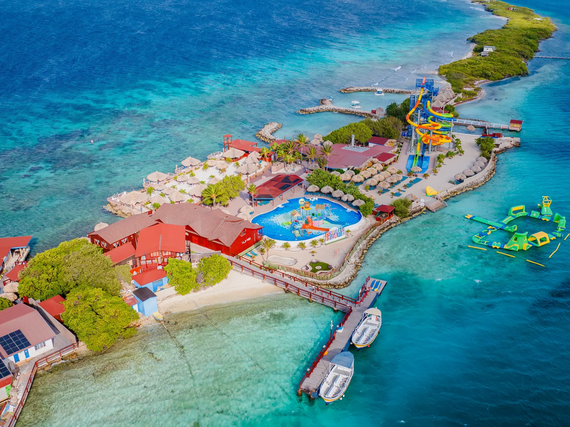 Aerial view of an island resort with pool, water slides, and docked boats.
