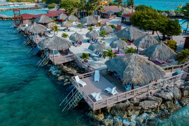 Island resort with straw huts by turquoise water and rocky shore.
